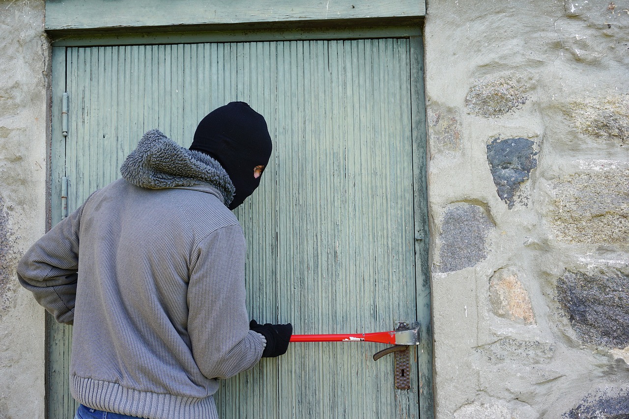 Ein vermummter Mann versucht mit einem Werkzeug eine Tür aufzubrechen