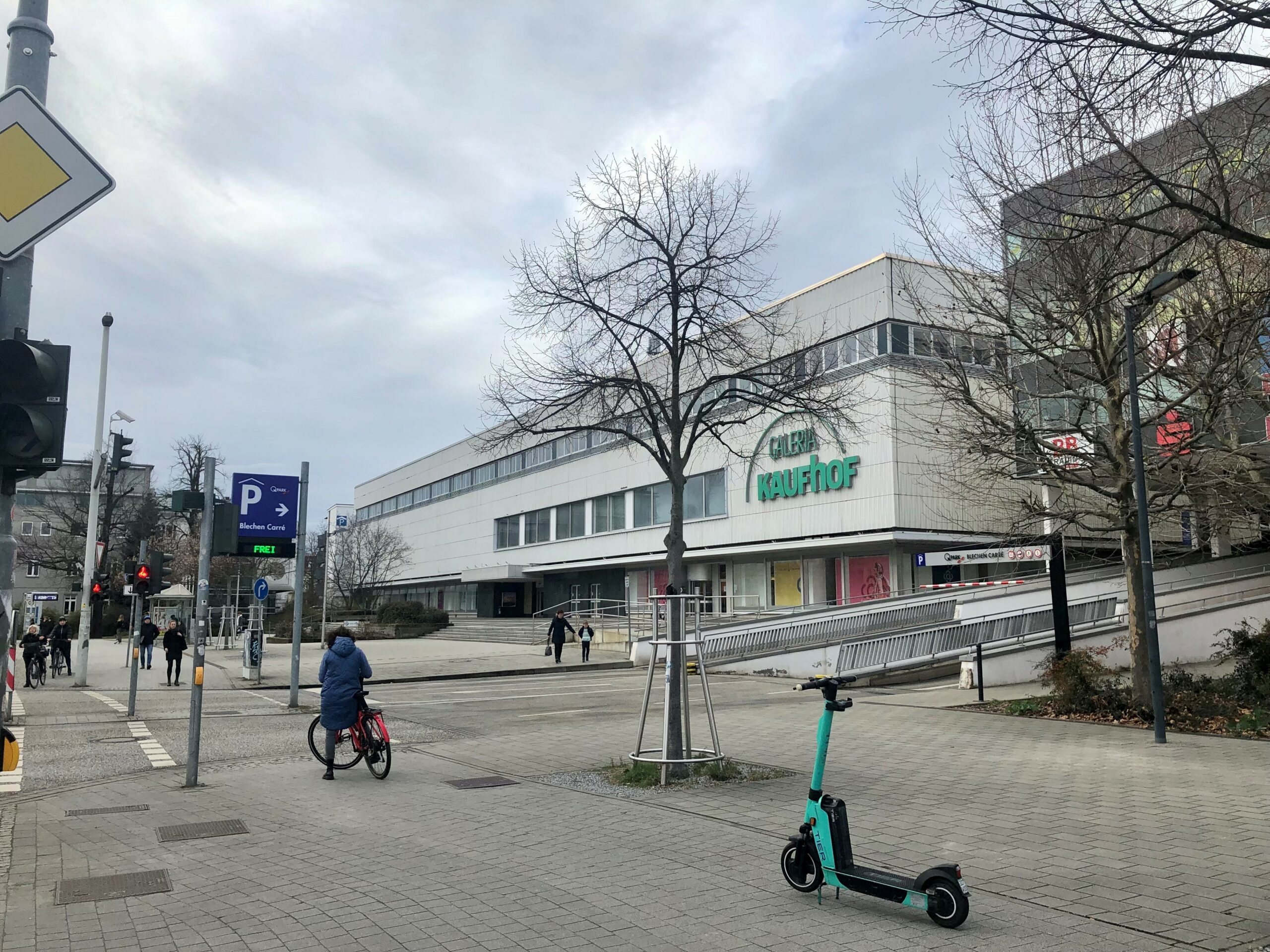 Ein E Scooter steht im Vordergrund. Er ist grün. Dahinter ist die alte Galeria Kaufhof Filiale in Cottbus zu sehen.