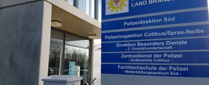 Polizeilogo auf Schild mit Schrift. Dieses steht vor dem Eingang am Polizeipräsidium