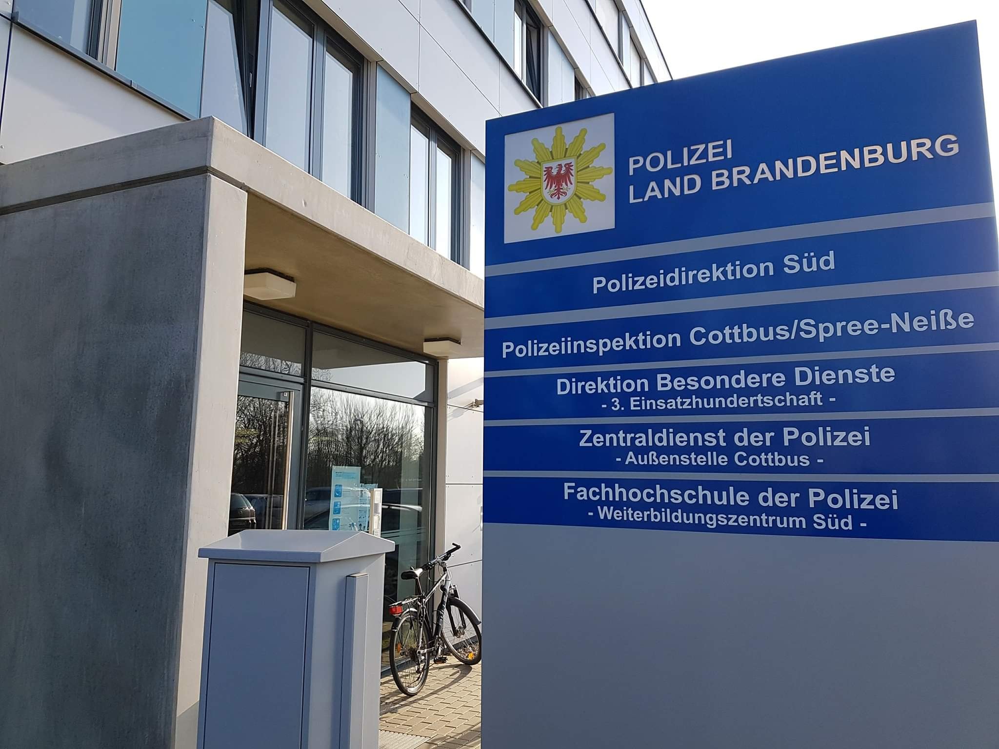 Polizeilogo auf Schild mit Schrift. Dieses steht vor dem Eingang am Polizeipräsidium