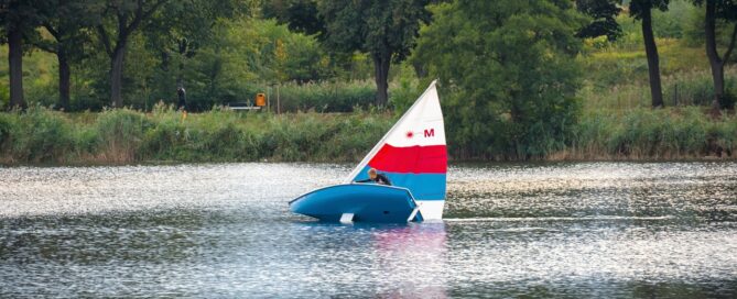 Ein Segelboot befindet sich auf dem Wasser. Das Segel ist rot weiß