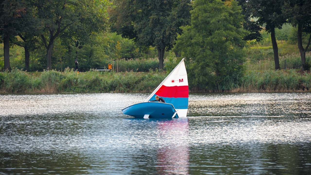 Ein Segelboot befindet sich auf dem Wasser. Das Segel ist rot weiß