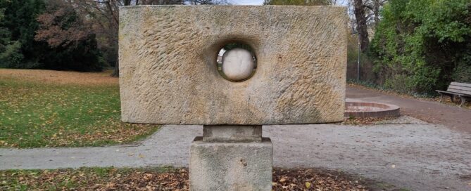 Zu sehen ist der Puschkinpark in Cottbus. Im Vordergrund steht eine Skulptur.