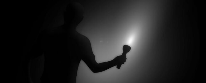 Ein Mann steht im dunkeln mit einer Taschenlampe in der Hand