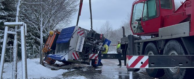 Auf dem Foto ist ein Streufahrzeug zu sehen. Es liegt im Straßengraben und wird von einem Kran geborgen.