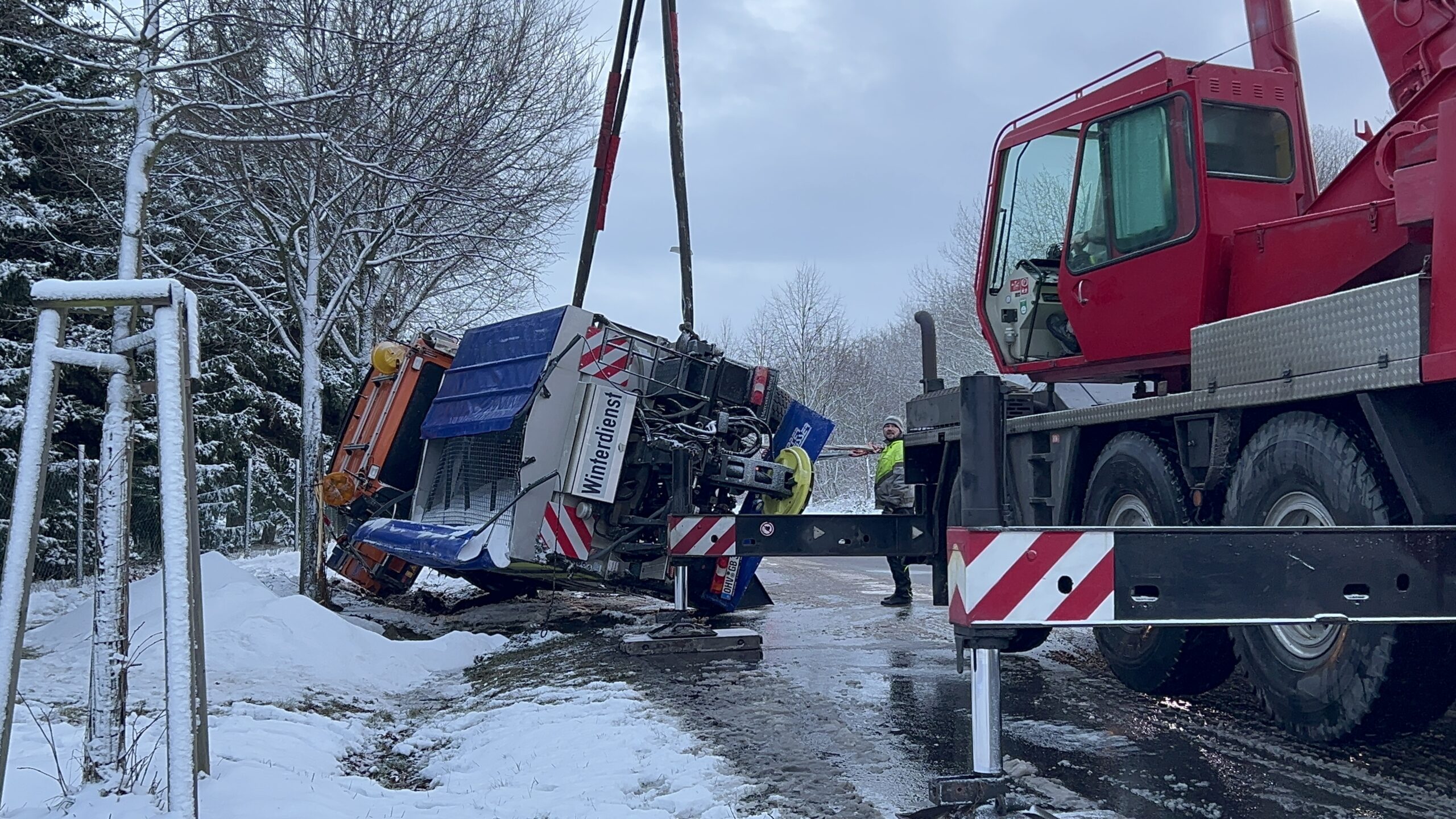 Auf dem Foto ist ein Streufahrzeug zu sehen. Es liegt im Straßengraben und wird von einem Kran geborgen.