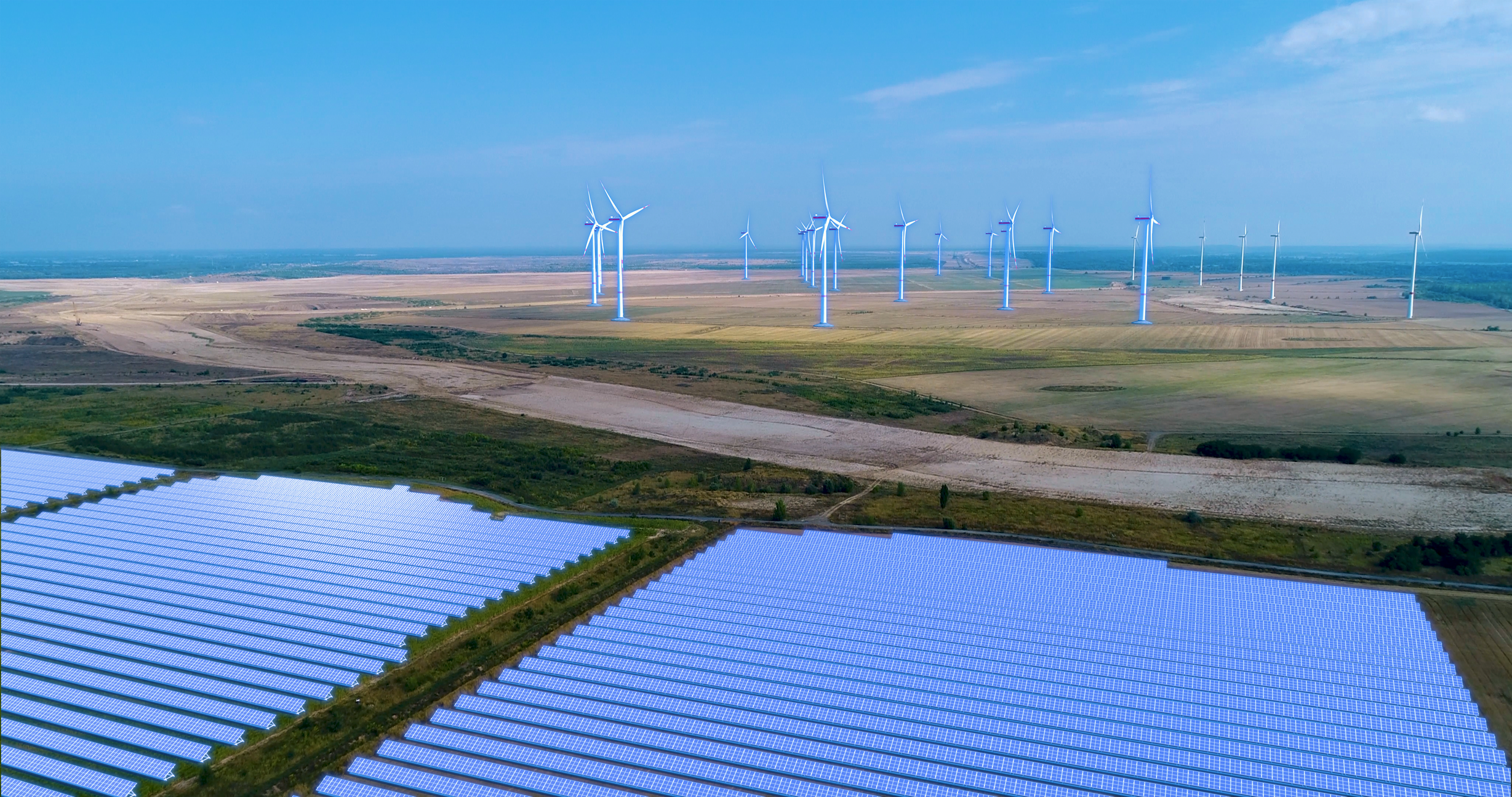 Windräder stehen im Hintergrund. Im Vorderfeld sind Solaranlagen zu sehen.