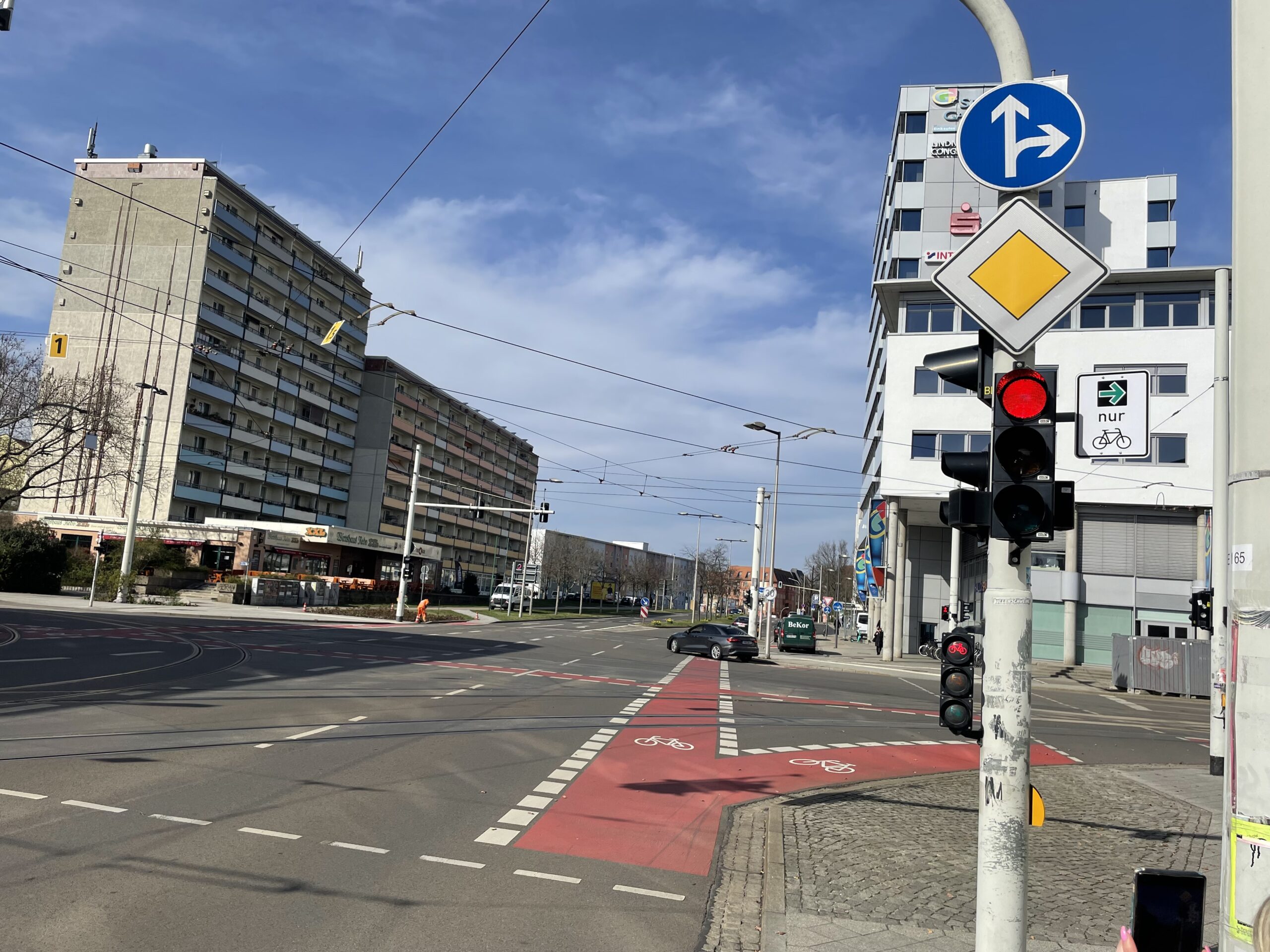 Wir befinden uns auf einer Kreuzung. Die Ampel ist rot. Es hängt ein grüner Pfeil für Radfahrer an der Ampel