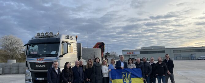 Das Foto zeigt die Delegation aus der Ukraine mit einer ukrainischen Fahne vor einem LKW.