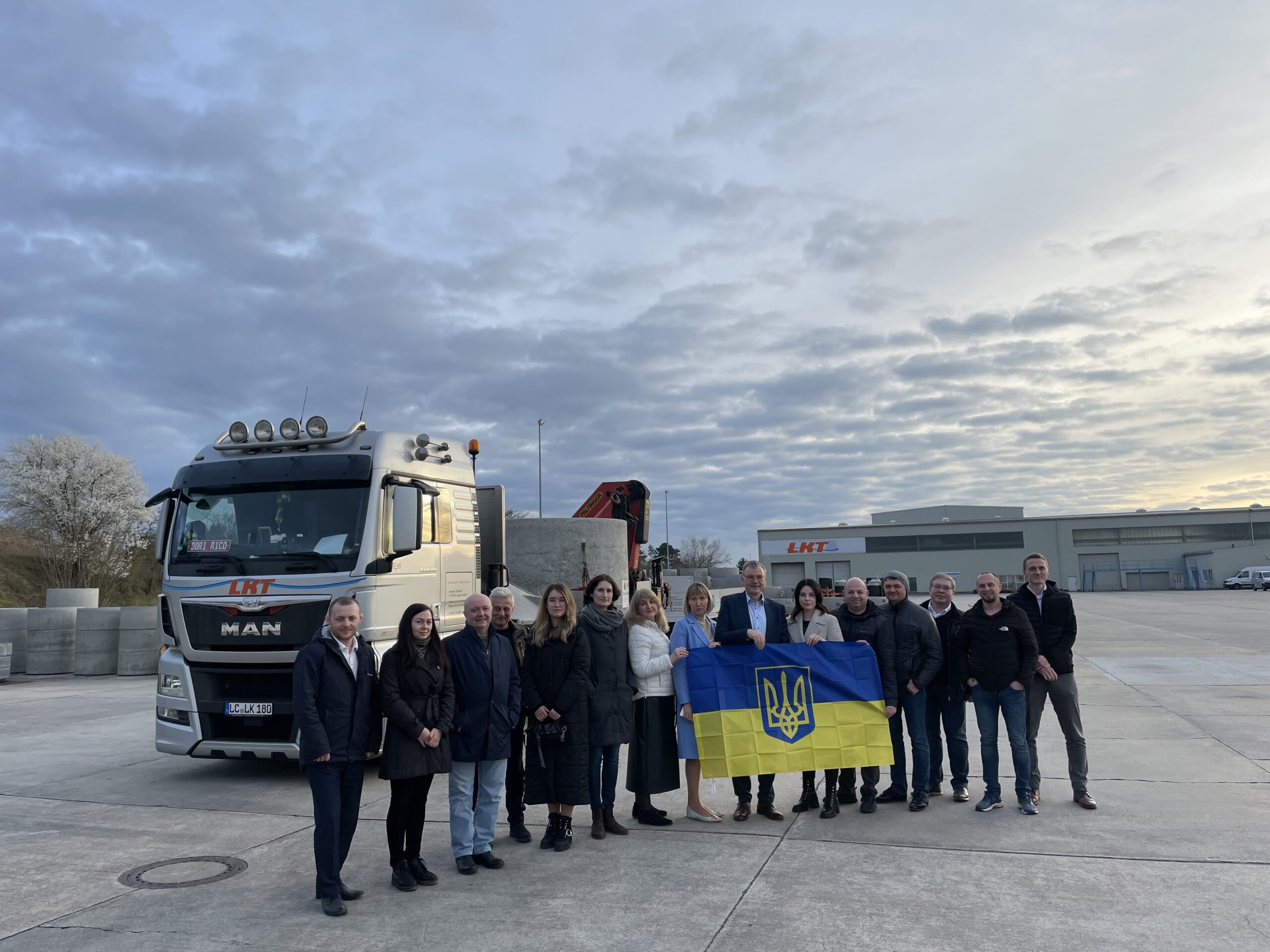 Das Foto zeigt die Delegation aus der Ukraine mit einer ukrainischen Fahne vor einem LKW.