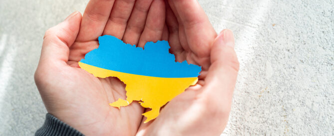 Das Symbolbild zeigt ein paar Hände, die einen Karton in Form und Farbe der Ukraine halten.