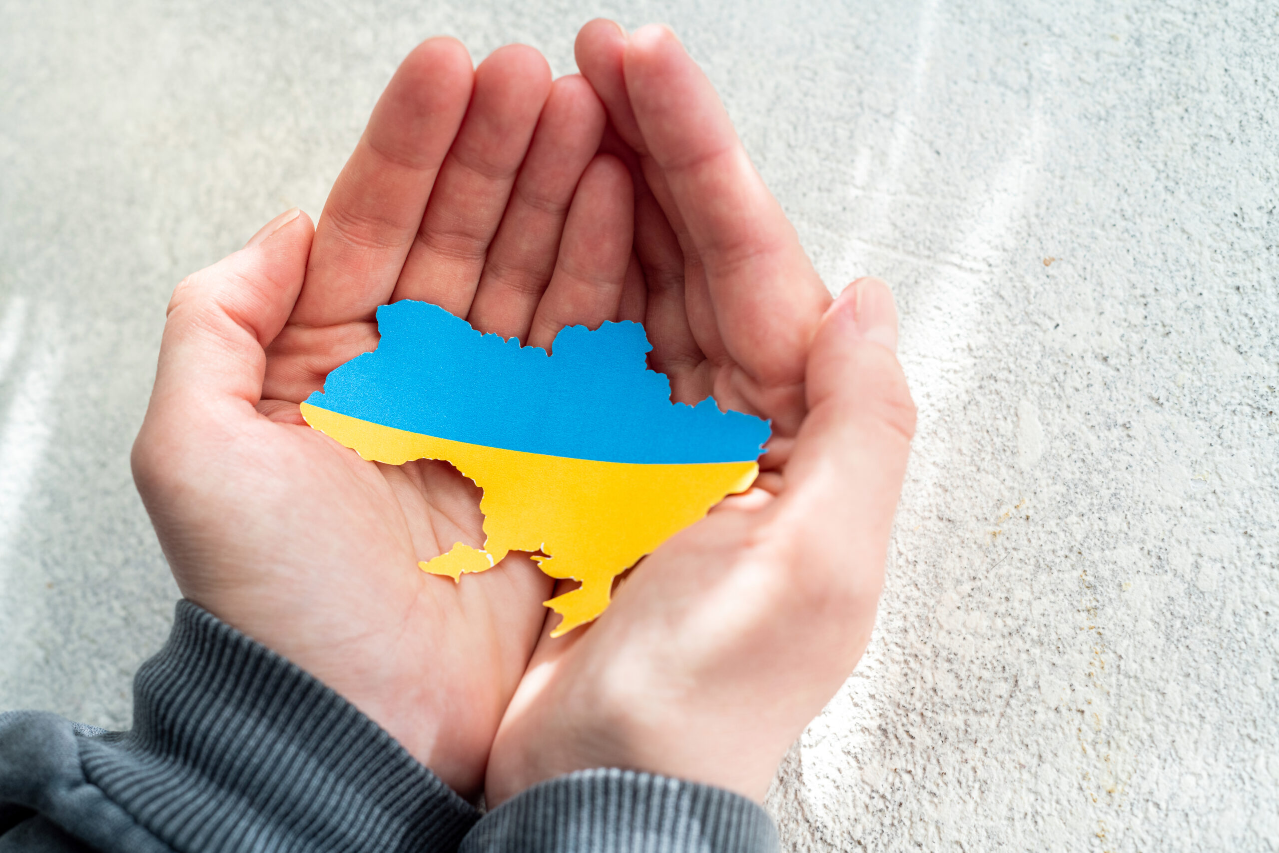 Das Symbolbild zeigt ein paar Hände, die einen Karton in Form und Farbe der Ukraine halten.