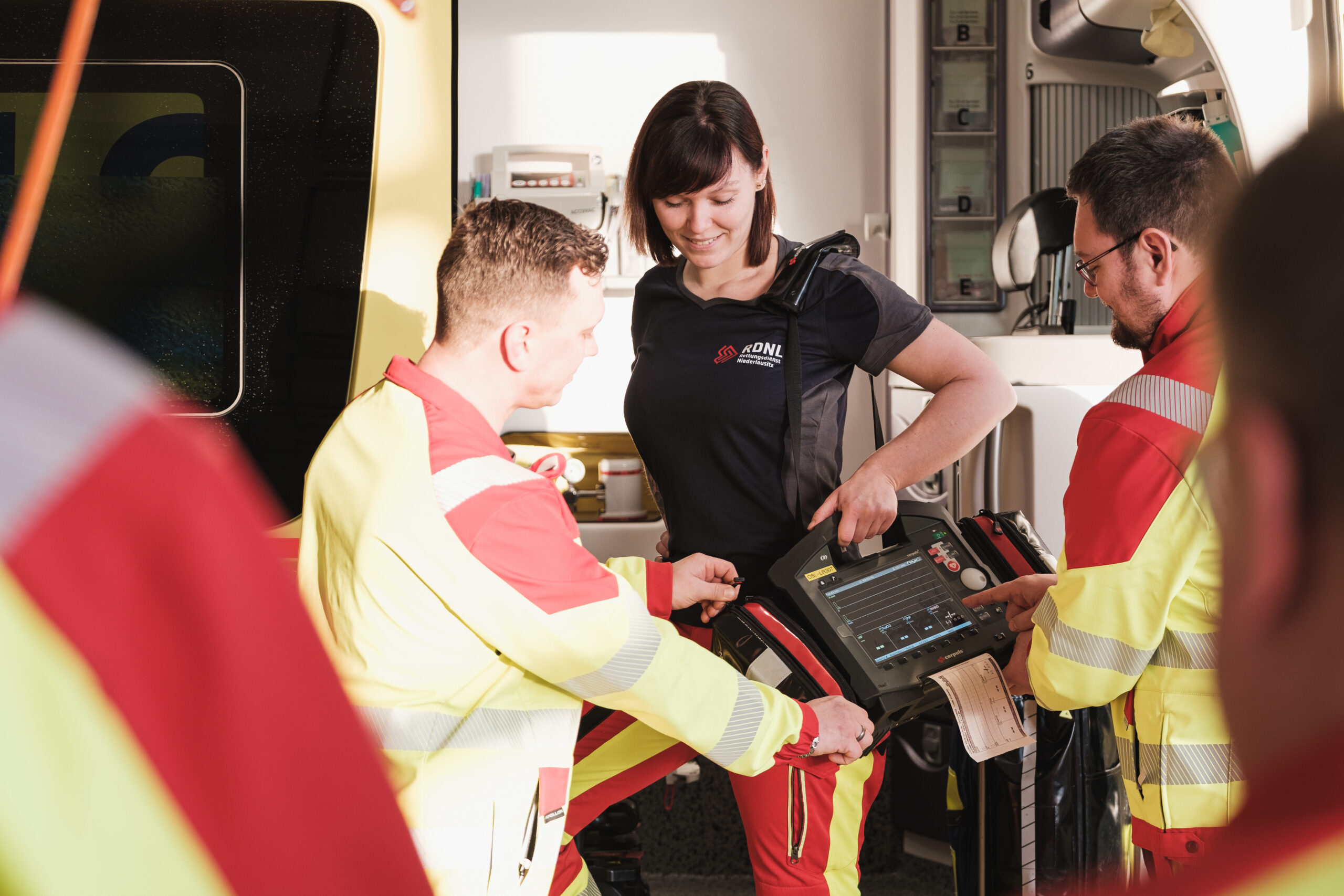 Das Foto zeigt ein technisches Gerät, das beim Rettungsdienst zum Einsatz kommt. Außerdem sind vier Mitarbeitende zu sehen.