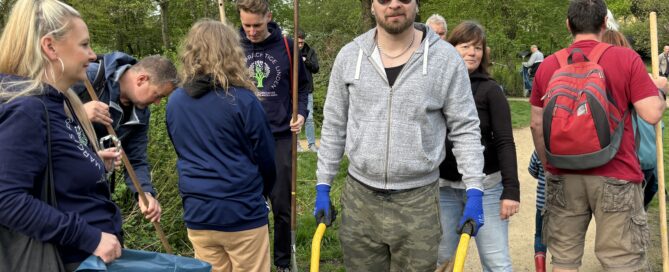 Gruppe von Menschen im Frühling mit Schubkarre, Harken und Müllbeuteln