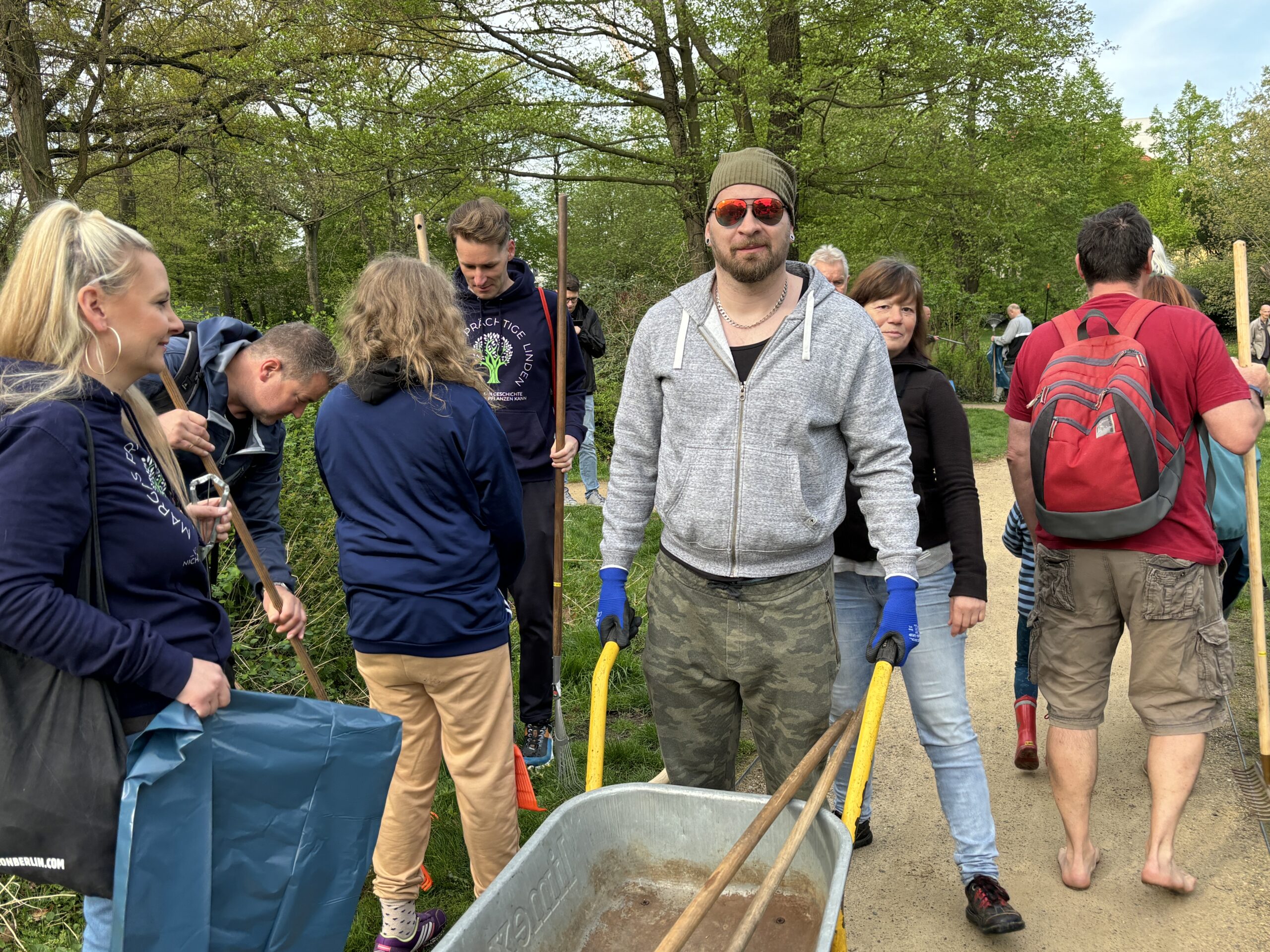 Gruppe von Menschen im Frühling mit Schubkarre, Harken und Müllbeuteln