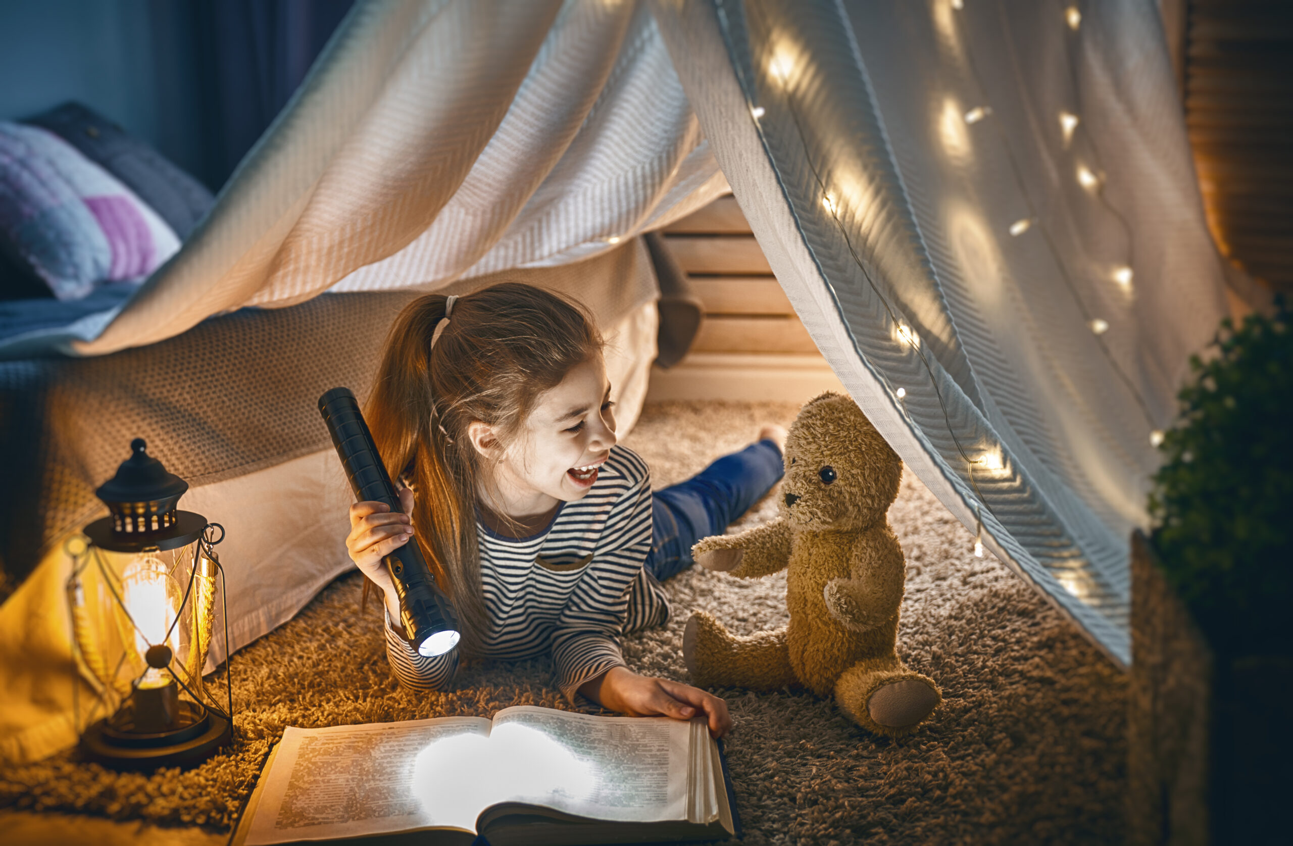 Das Foto zeigt ein lachendes Mädchen, das mit einer Taschenlampe ein Buch liest.