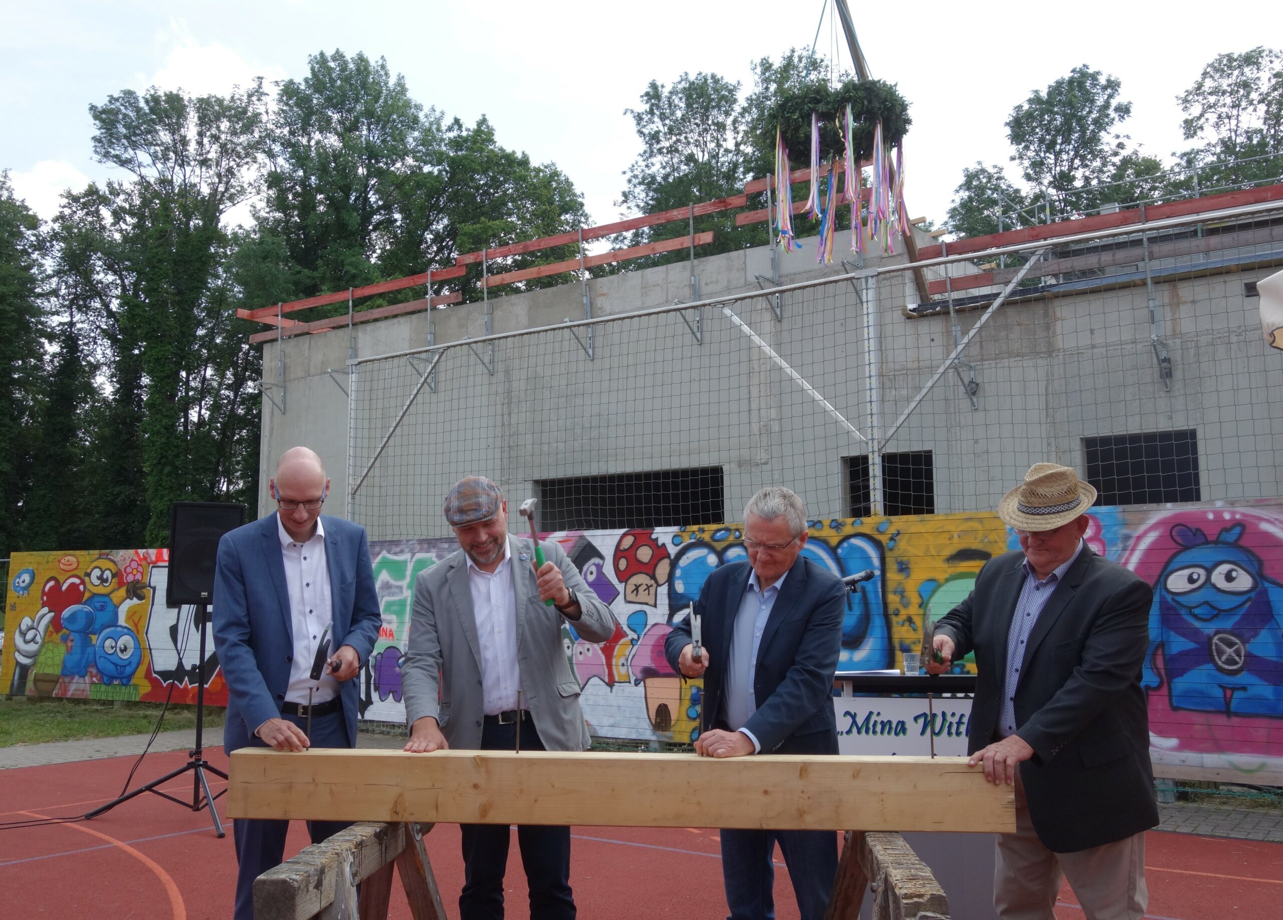 47_Richtfest Kultur- und Sportzentrum_Foto K.Möbes Carsten Billing, Dezernent für Wirtschaft, Finanzen, Ordnung, Sicherheit und Verkehr des Landkreises Spree-Neiße/Wokrejs Sprjewja-Nysa, Amtsdirektor Tobias Hentschel, Markus Mandel, Schulleiter der Grund- und Oberschule „Mina Wikojc“ und Bürgermeister Hans-Jürgen-Dreger (v. l.) vollziehen den symbolischen Richtfest-Akt und schlagen die letzten Nägel ein.