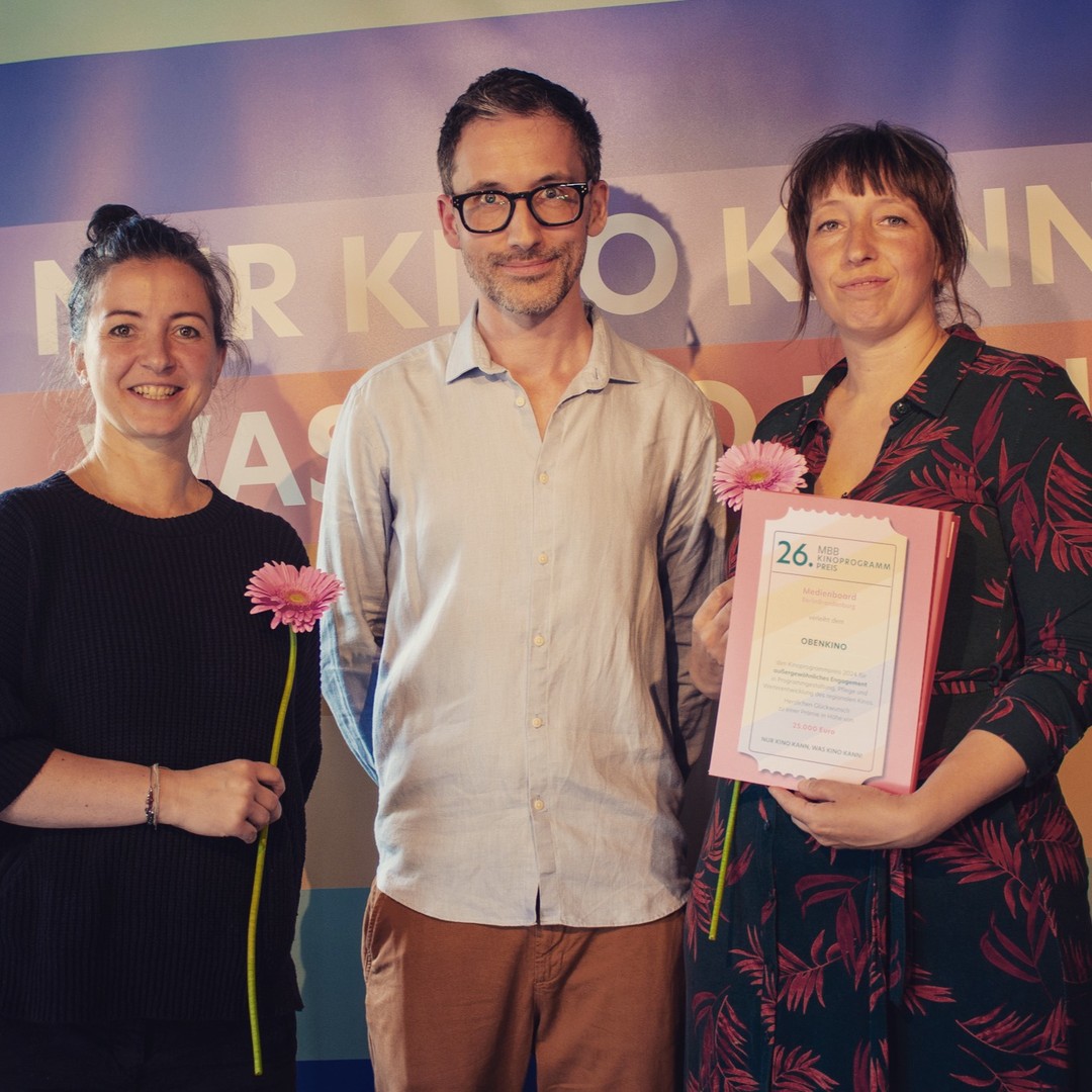 Obenkino Drei Menschen stehen nebeneinander und halten einen Preis in der Hand