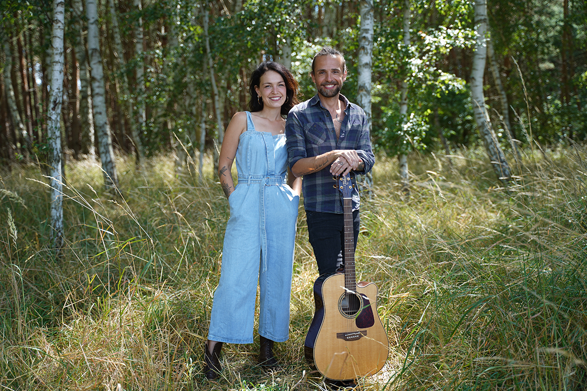 Mann und Frau stehen mit einer Gitarre im Wald