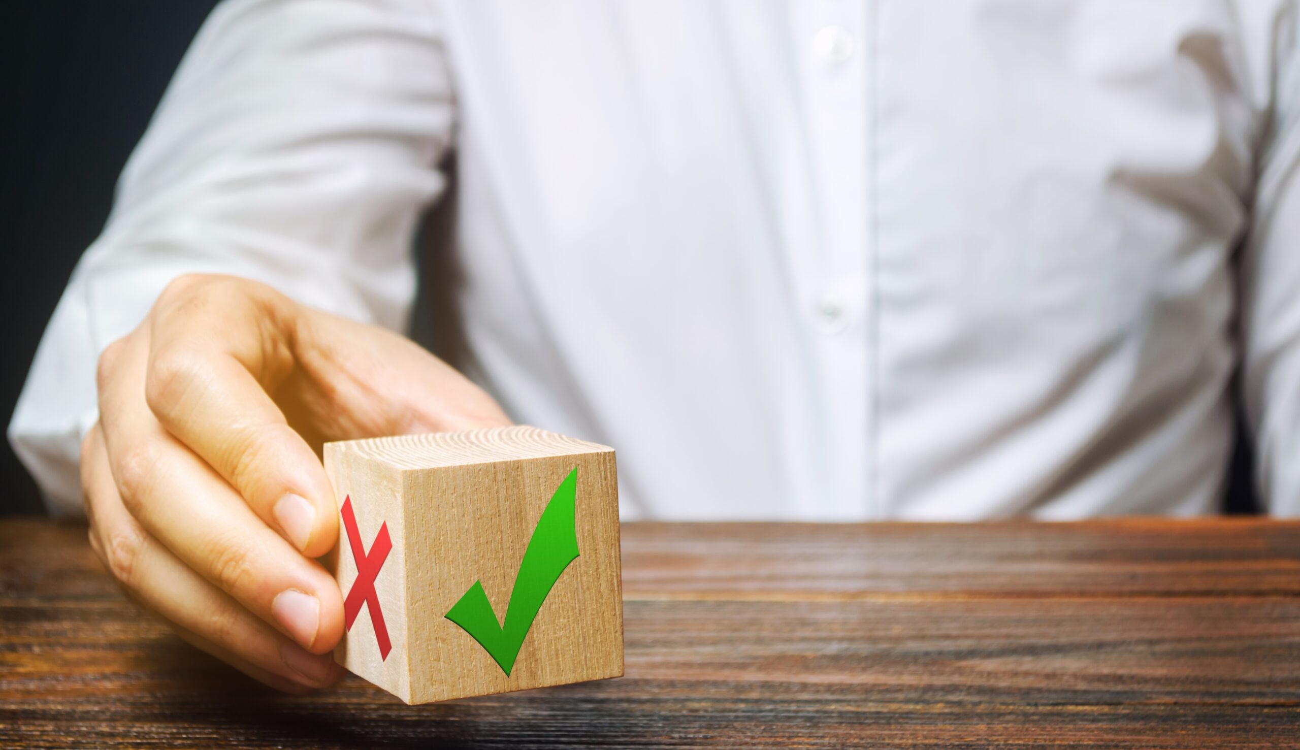 choice-2023-11-27-05-20-37-utc Das Foto zeigt symbolisch für die Wahl eine Person, die ein Holzklötzchen mit einem grünen Haken und einem roten Kreuz in der Hand hält.