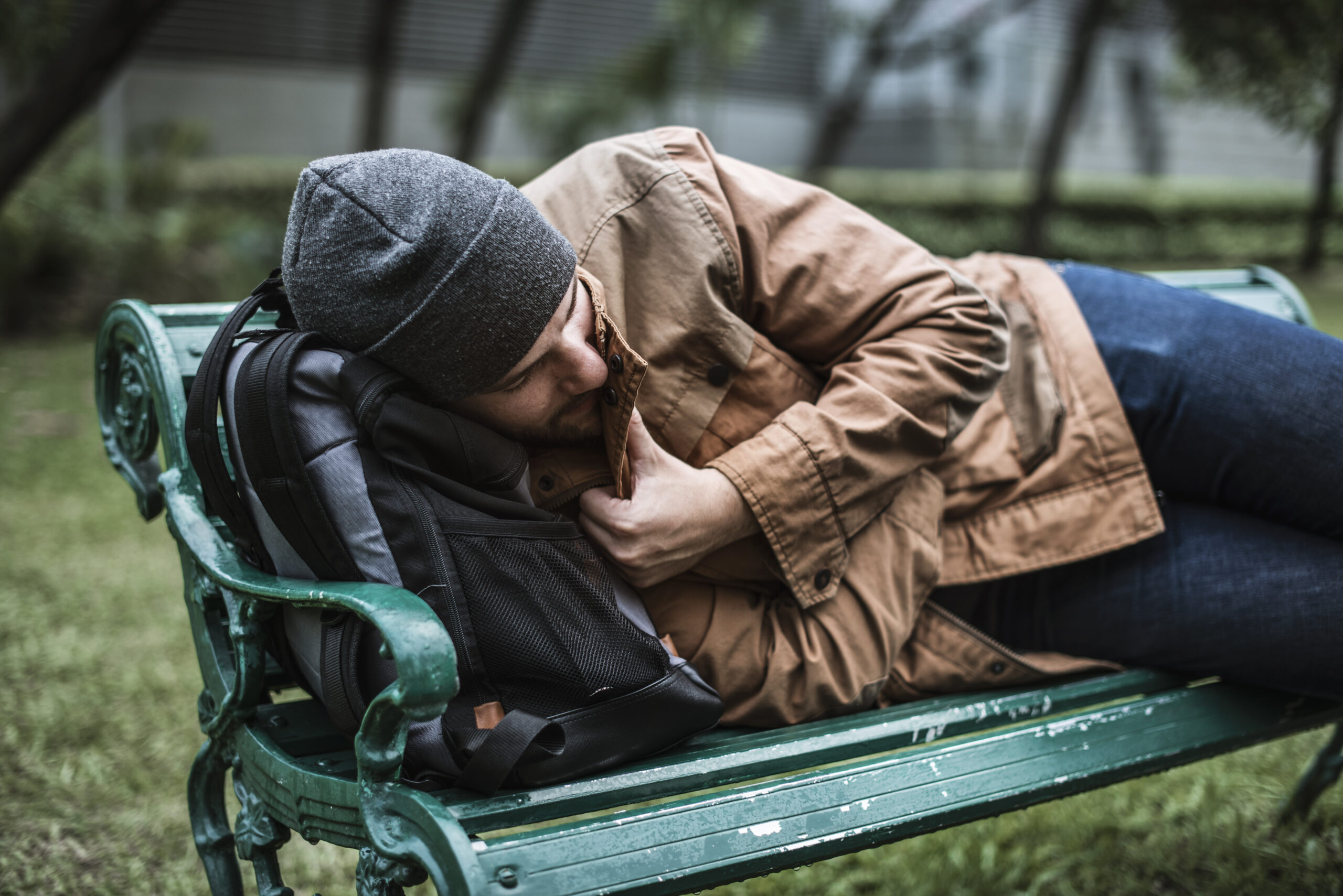 Homeless Adult Man Sleeping on Bench in The Park Ein Obdachloser liegt auf einer Parkbank.