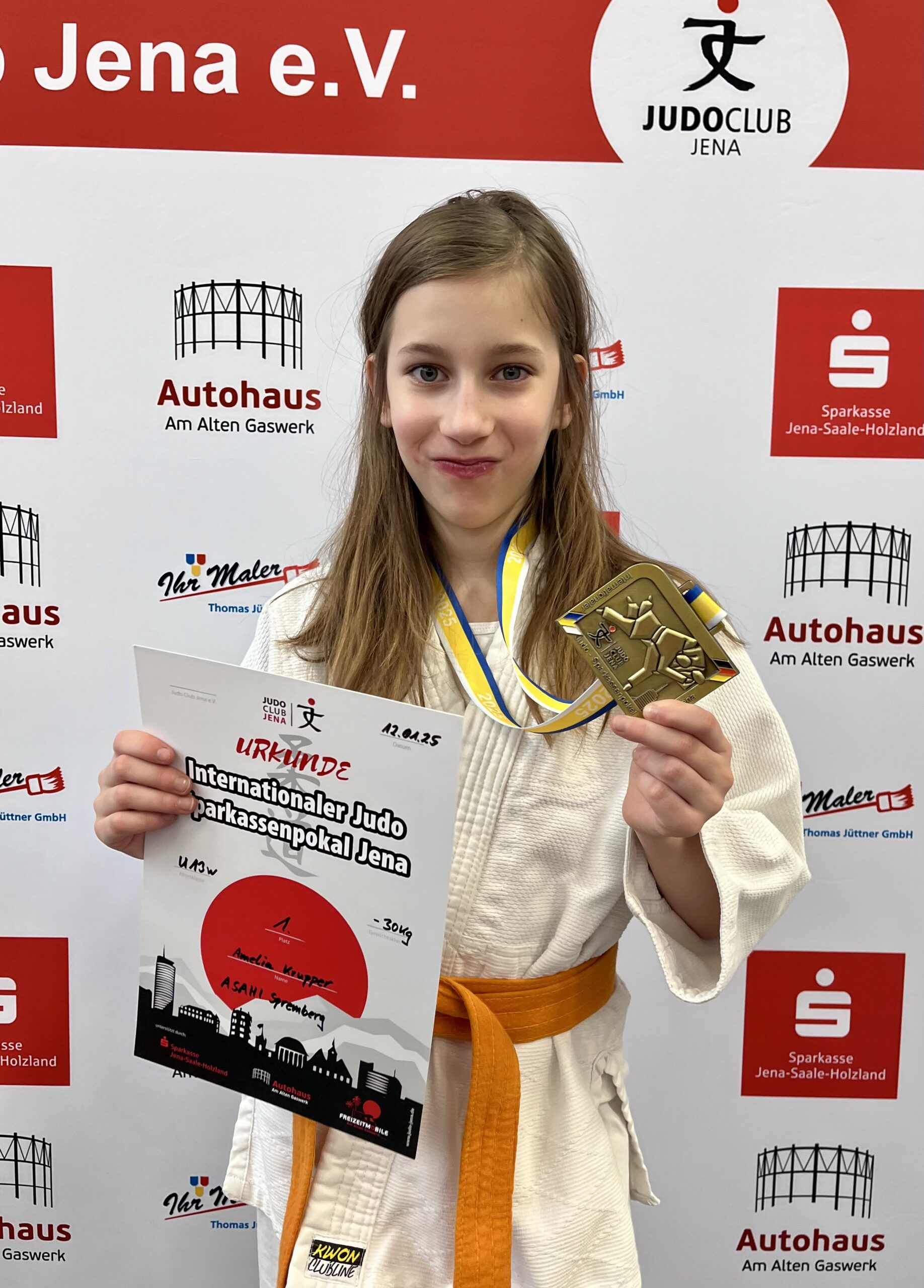 Amelia Ein Mädchen in Judoklamotten hält eine Goldmedaille nach oben