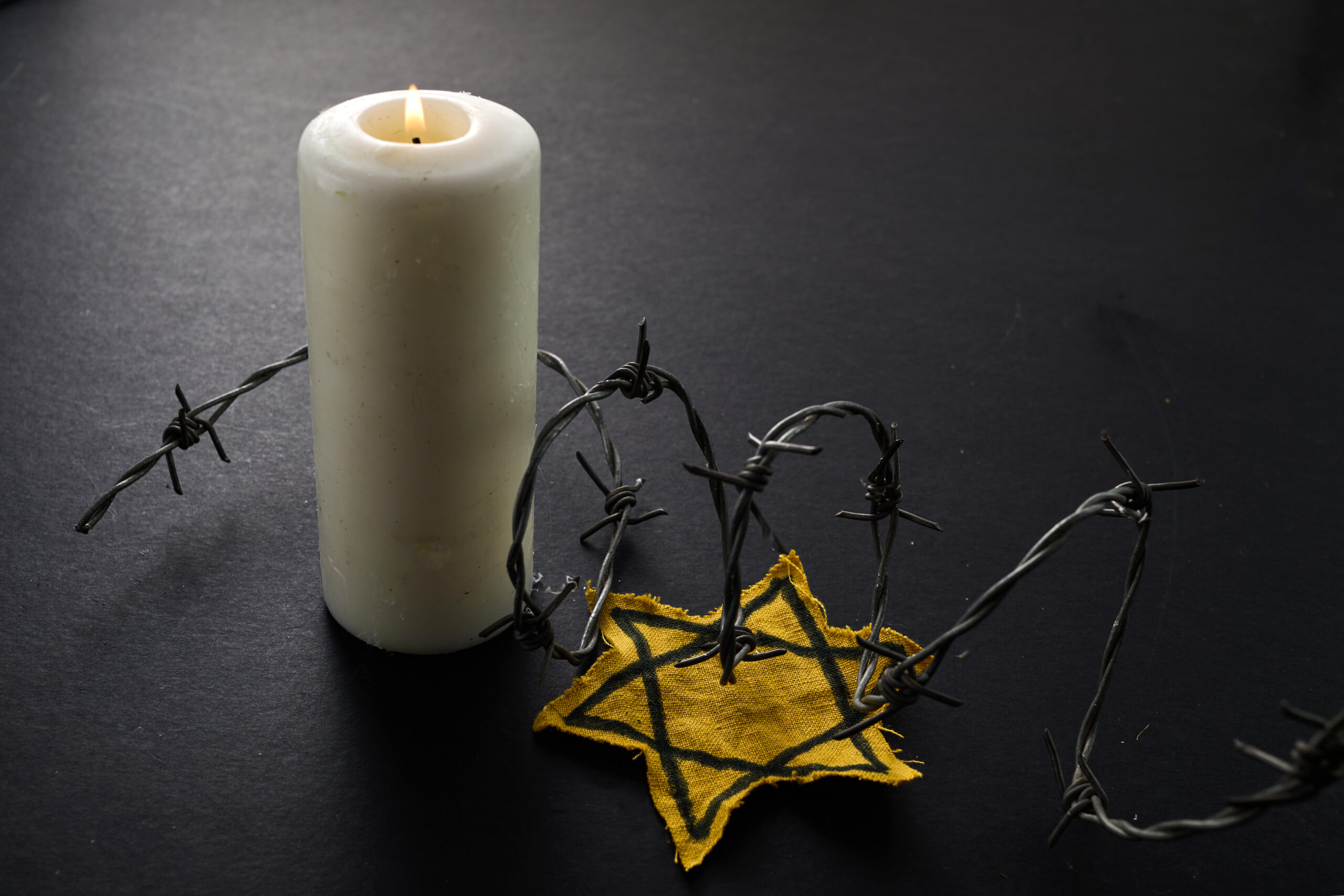 Symbolbild zum Gedenken an den Holocaust mit Kerze, Stacheldraht und gelbem Stern.