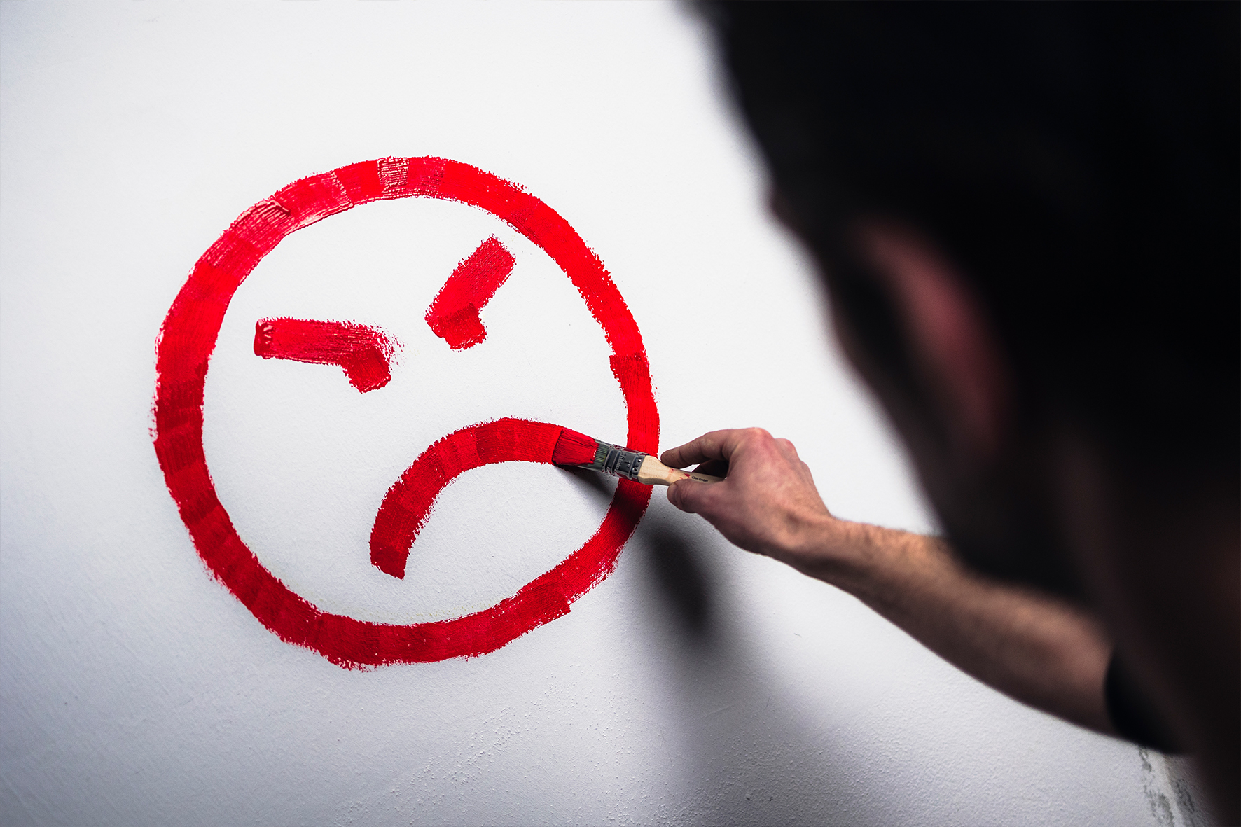 Maler mit Wut-Emoji Ein Maler zeichnet mit roter Farbe ein wütendes Emoji.