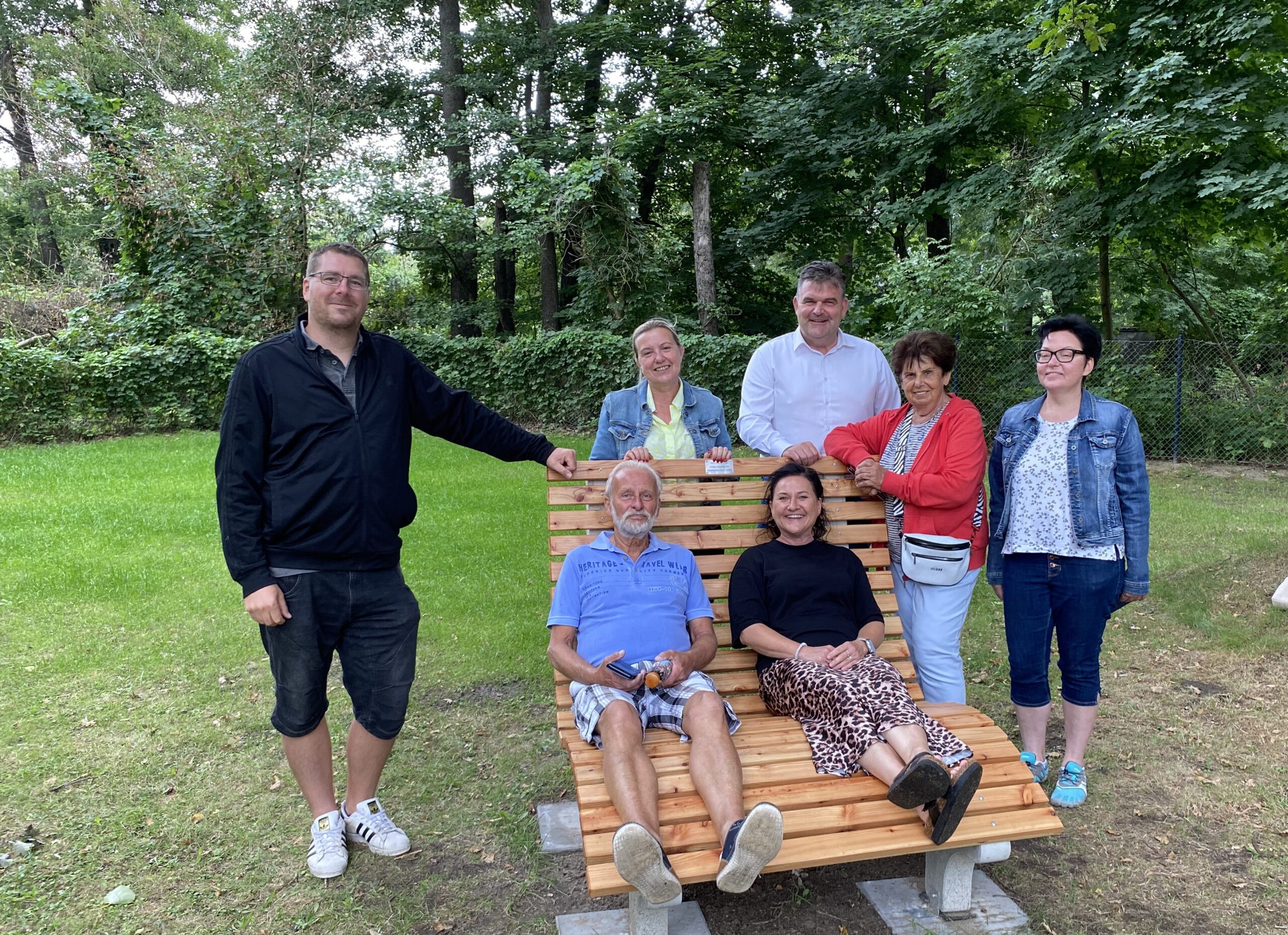 Bank im Freibad kl.1 Menschen stehen um Holzbänke herum
