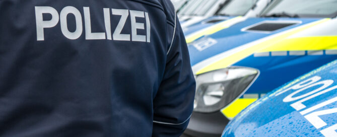Ein Polizist in Polizeijacke steht vor Streifenwagen