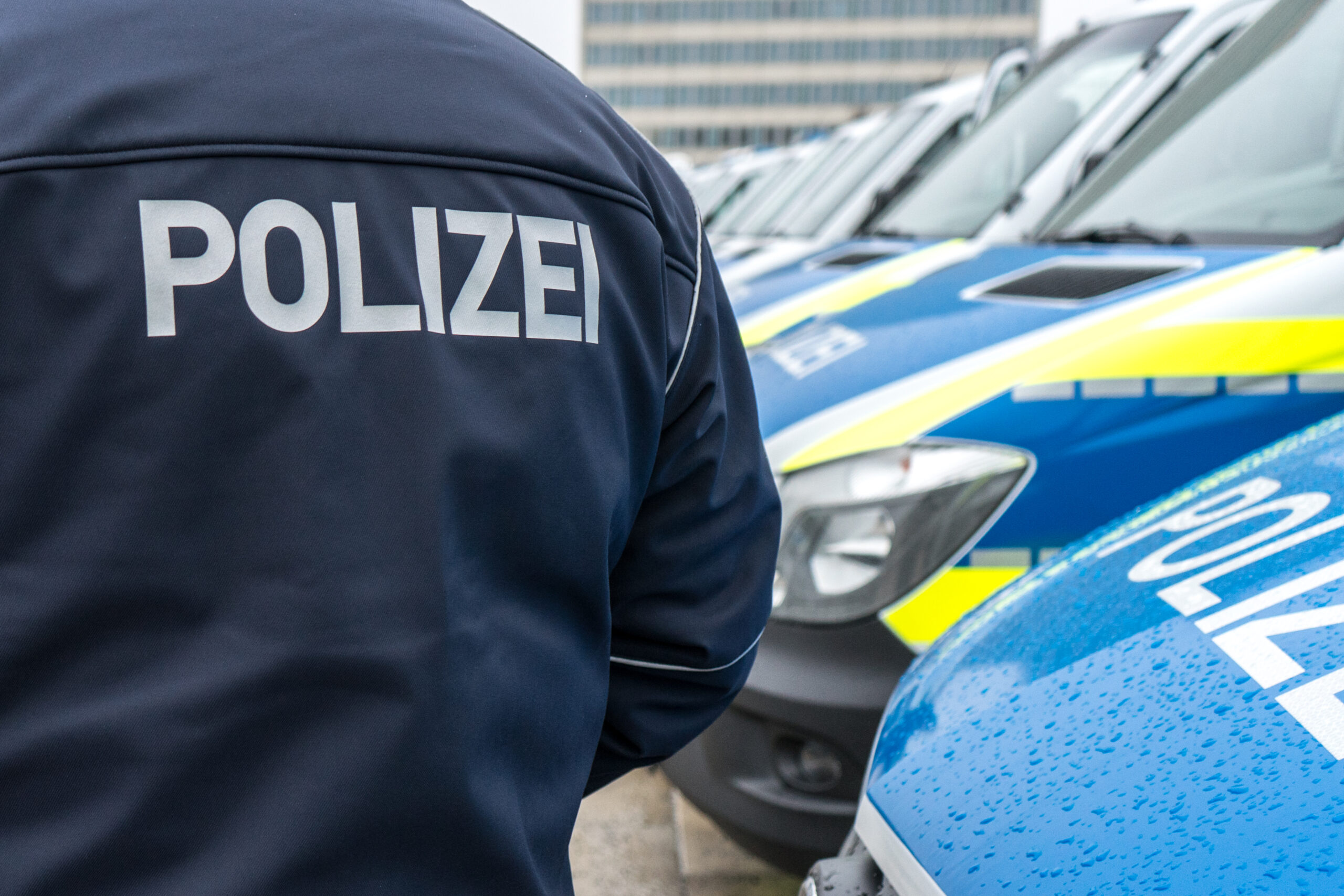 Polizei Ein Polizist in Polizeijacke steht vor Streifenwagen