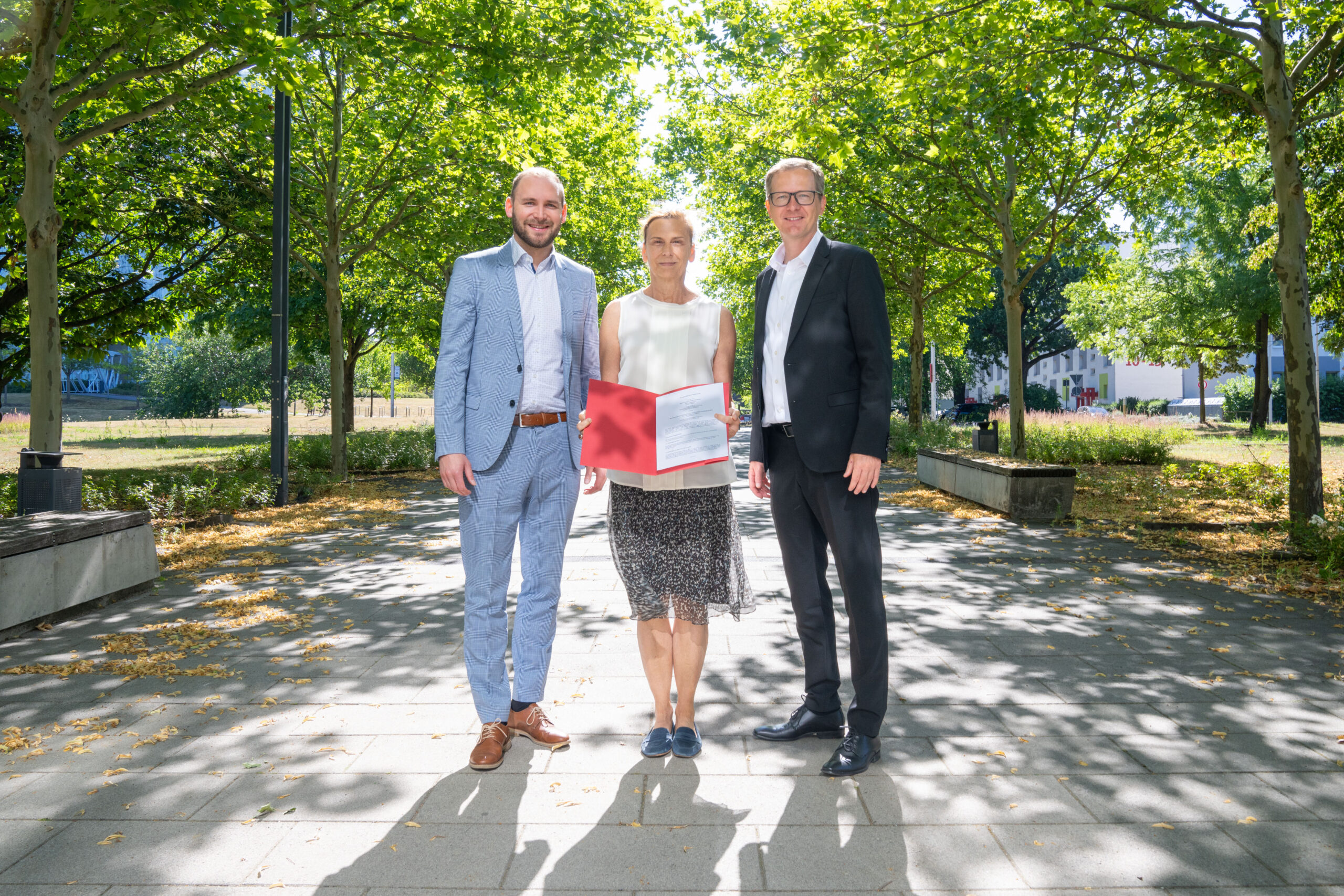 Sparkasse BTU Drei Menschen stehen im grünen und halten einen Vertrag hoch