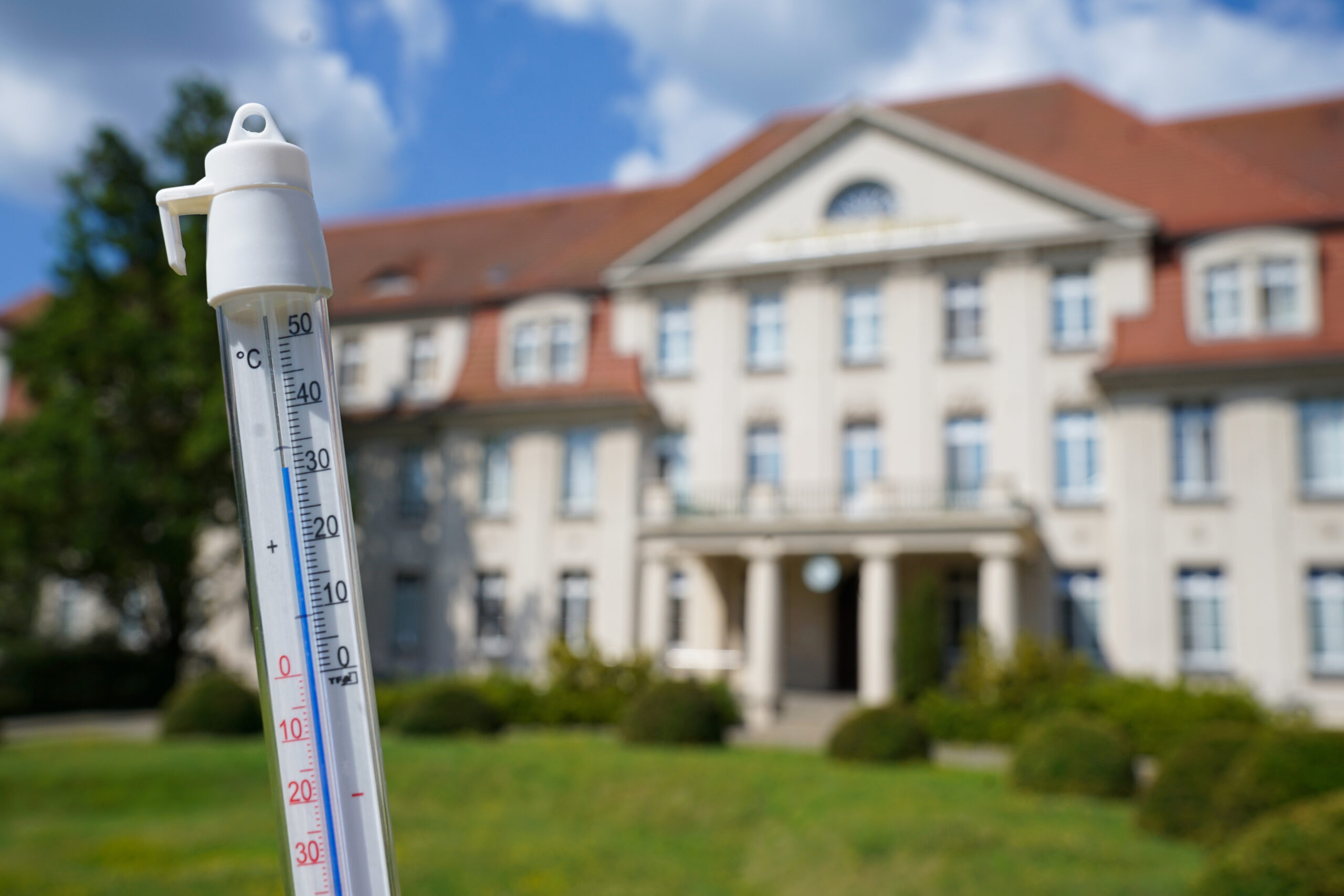 Thermometer wird vor ein Geäude in die Luft gehalten