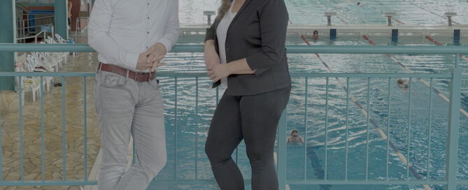 Das Bild zeigt zwie Menschen die im Schwimmbad stehen