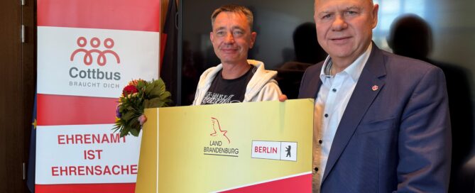 Zwei Männer stehen in einem Raum und halten eine Karte hoch