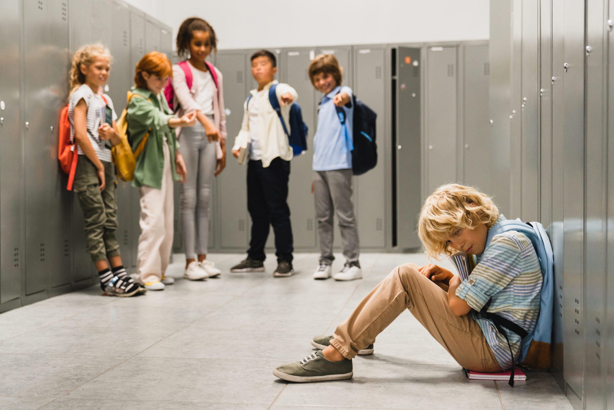 Sad crying schoolboy pupil sitting on the floor at the school hall while his classmates teenagers Fotocollage Kinder die andere Kinder mobben sind darauf zu sehen