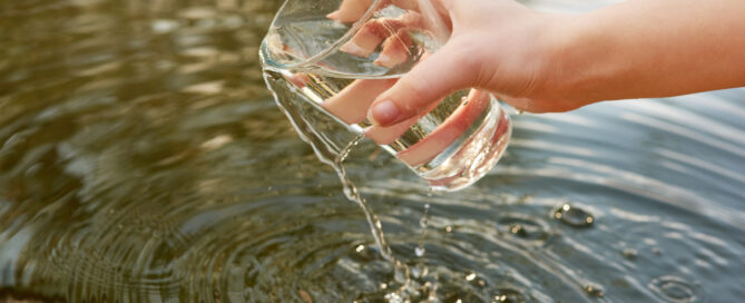 Ein Wasserglas wird in einen See gehalten.