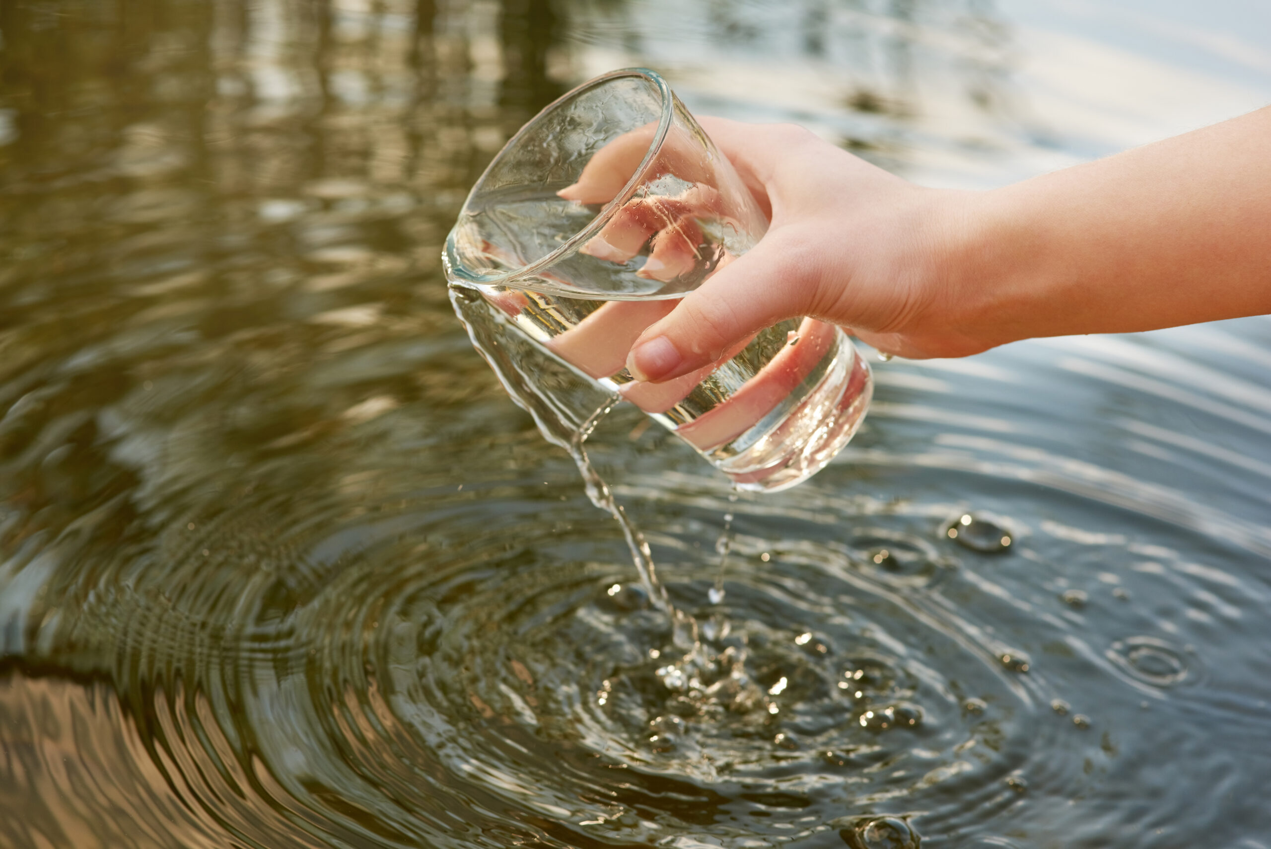 Ein Wasserglas wird in einen See gehalten.