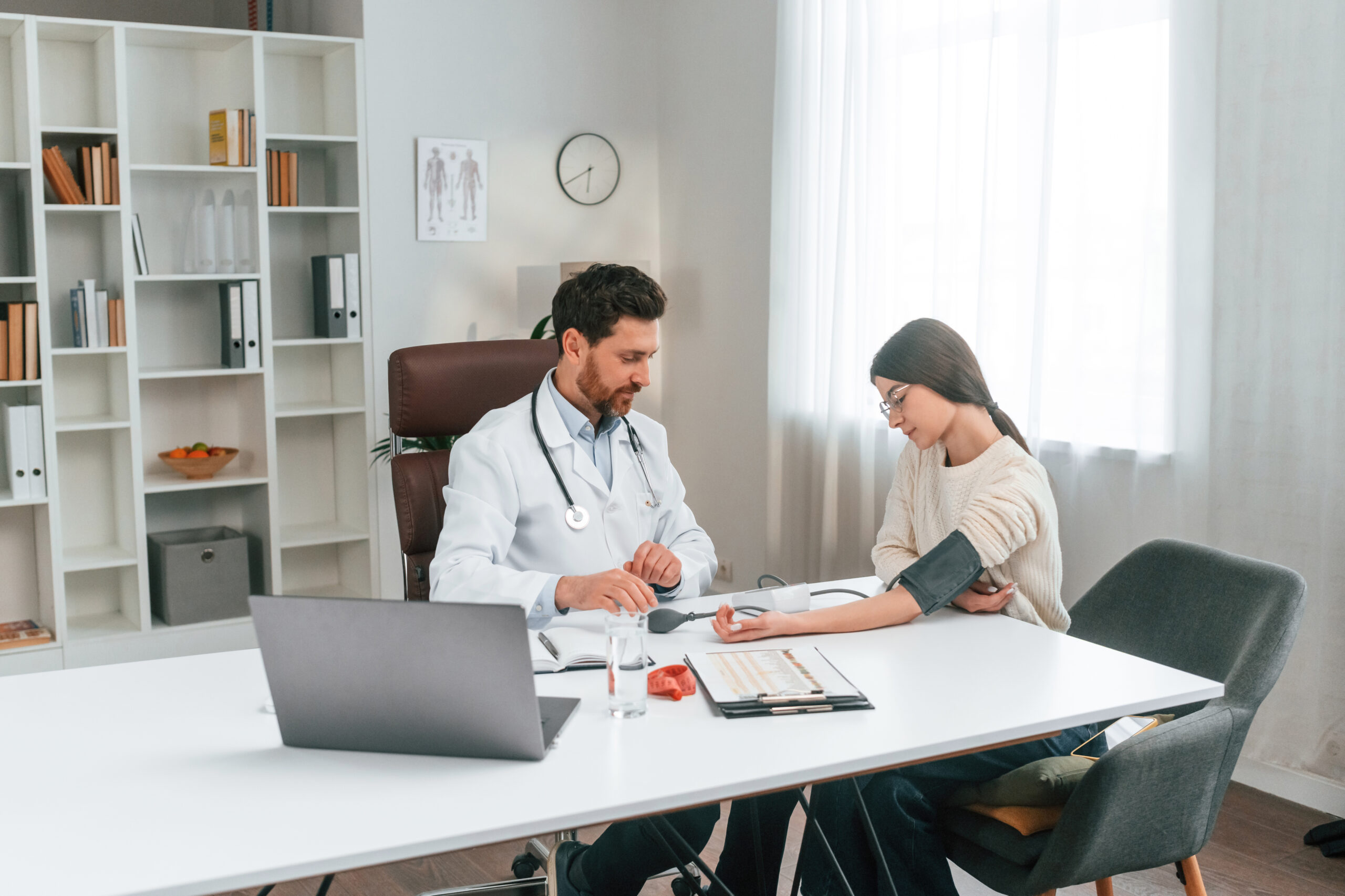 Measuring blood pressure. With woman. Doctor in formal clothes is working in the cabinet Das Foto zeigt einen Arzt in der Praxis der den Blutdruck einer Patientin misst.