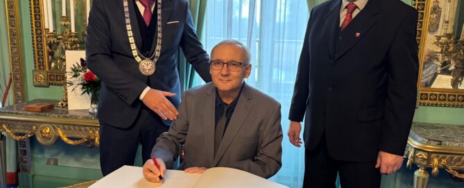 Drei Personen sind auf einem Bild zu sehen. Einer schreibt sich in das Goldene Buch der Stadt Cottbus ein