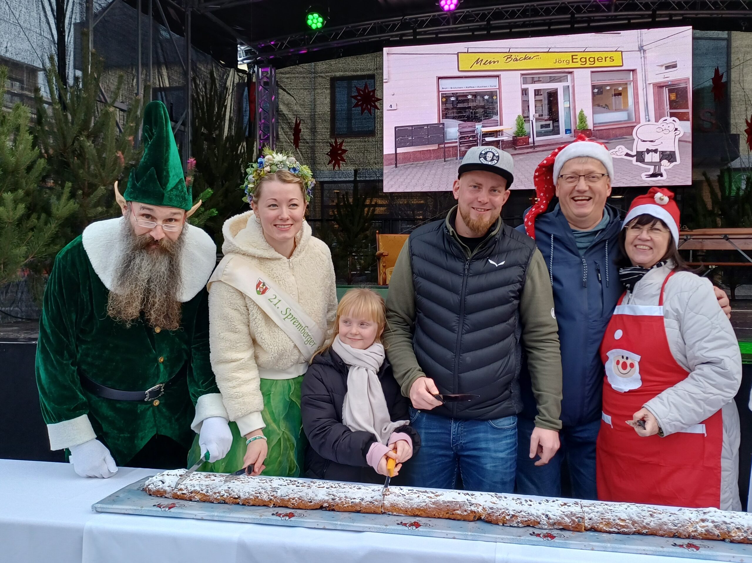 Menschen stehen nebeneinander und schneiden einen Stollen an