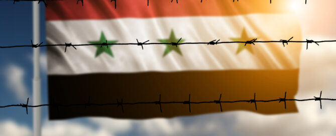 Das Symbolbild zeigt die Flagge von Syrien , die hinter Stacheldraht weht.