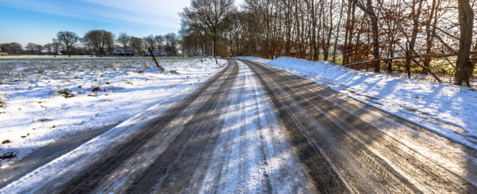 Eine Landstraße mit vereister Fahrbahn und Schnee.