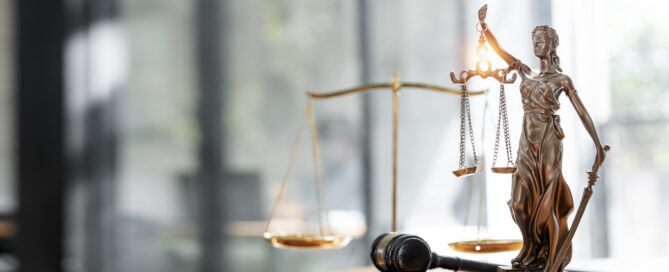 Das Symbolbild zeigt einen Schreibtisch mit einer Statue von Justitia, einer Waage und einem Richterhammer.