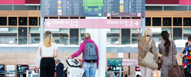 Pssagiere stehen vor der Anzeigetafel am Flughafen