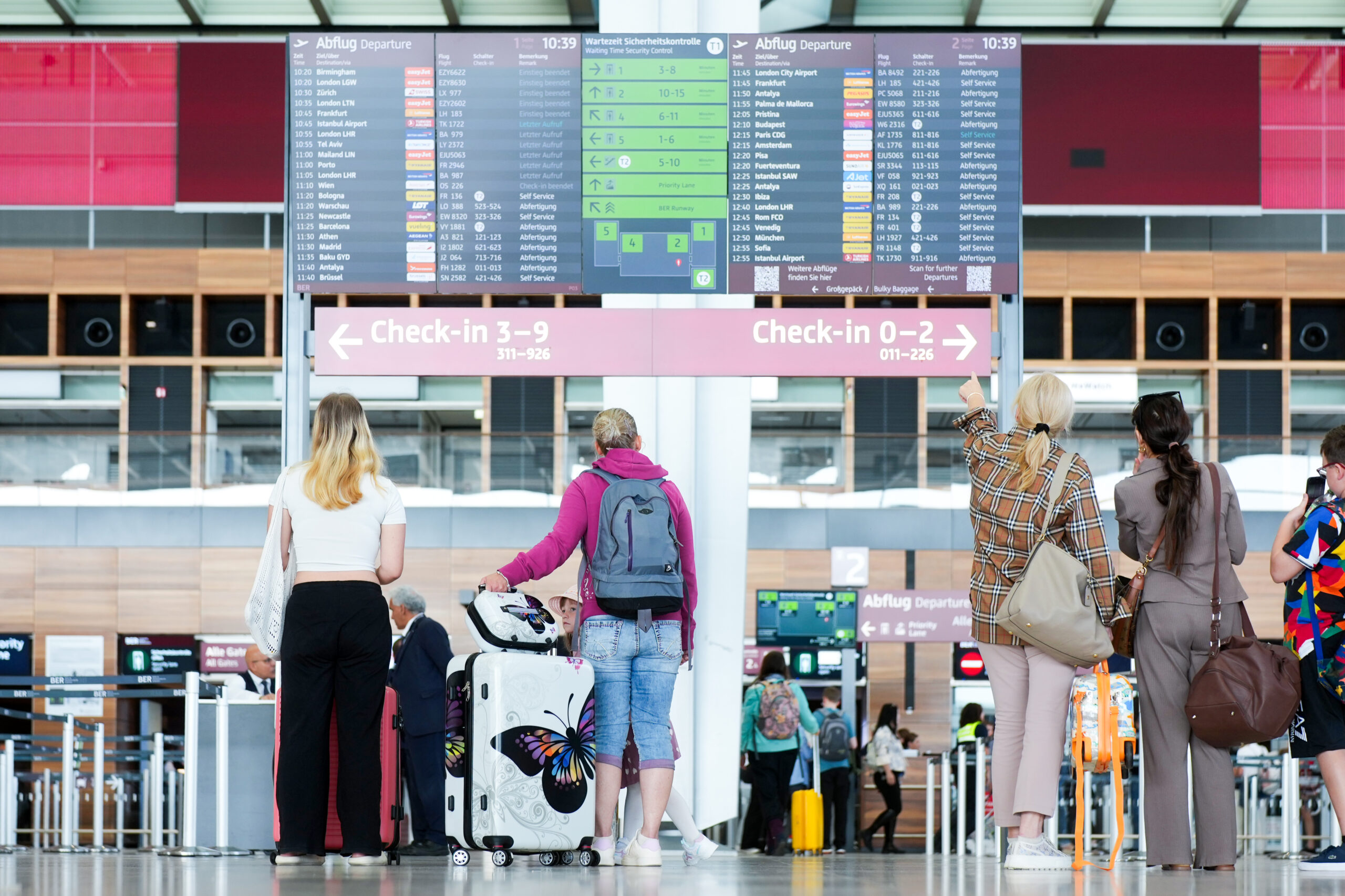 Pssagiere stehen vor der Anzeigetafel am Flughafen