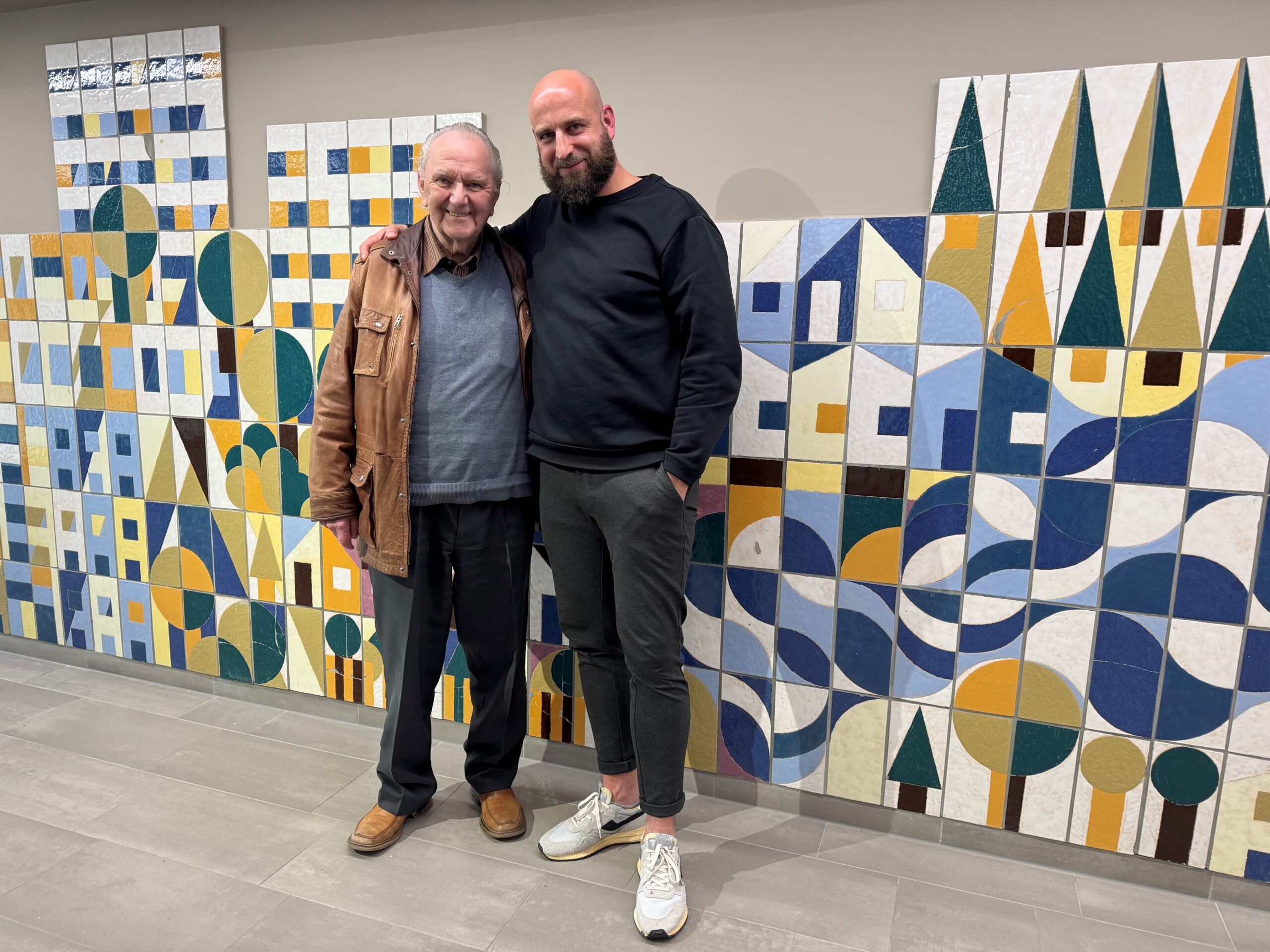 Zwei Personen stehen vor einer Mosaikwand