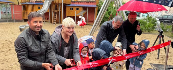 Menschen schneiden ein rotes Band durch und eröffnen Spielplatz