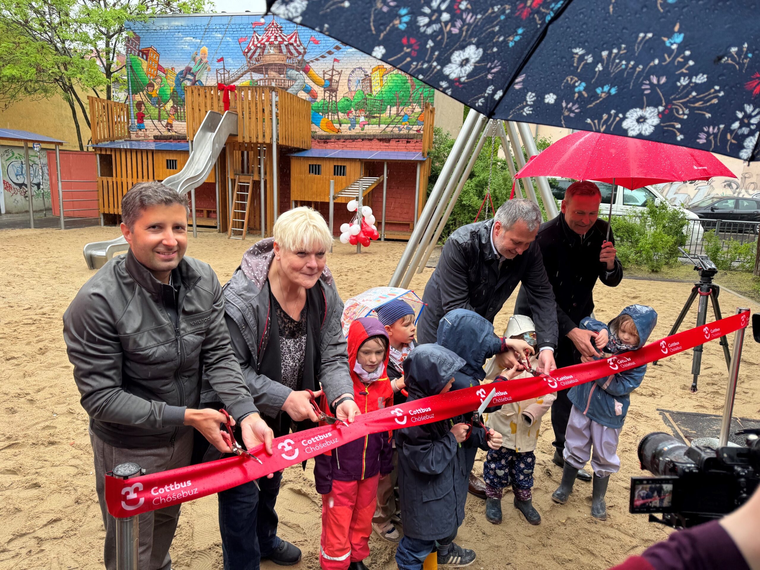 Menschen schneiden ein rotes Band durch und eröffnen Spielplatz