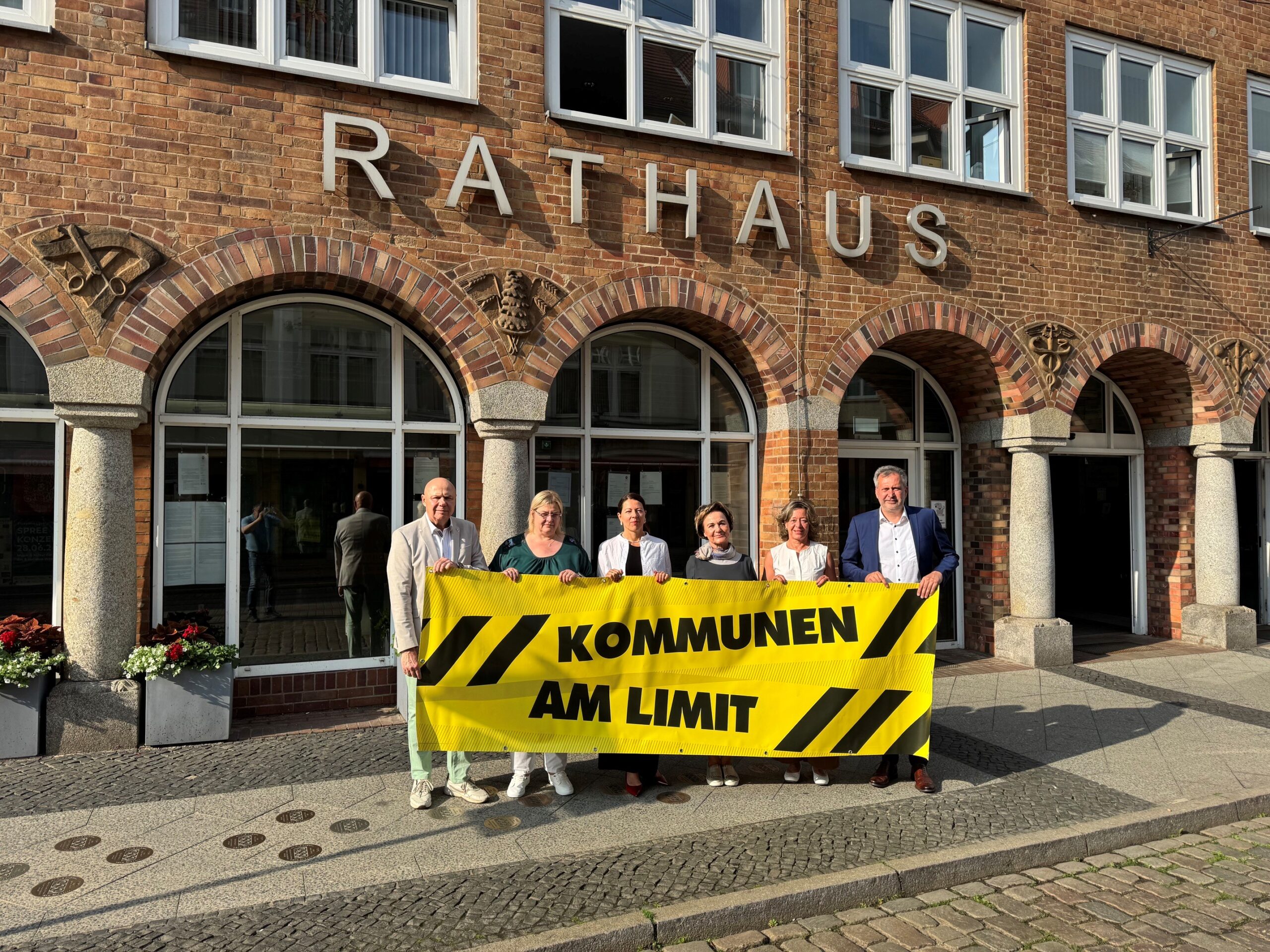 2026_06_22_KommunenamLimit_2 Vor dem Cottbuser Rathaus stehen Menschen und halten ein Plakat hoch